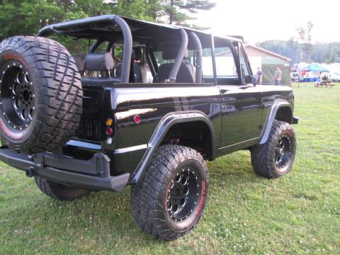 1979 Ford Bronco - This black Ford Bronco is shown from the rear quarter angle, parked on a grassy field with tents in the background.
