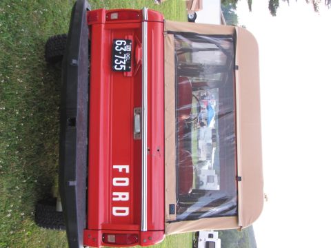 1979 Ford Bronco - This red Ford Bronco features a tan soft top and a visible license plate.