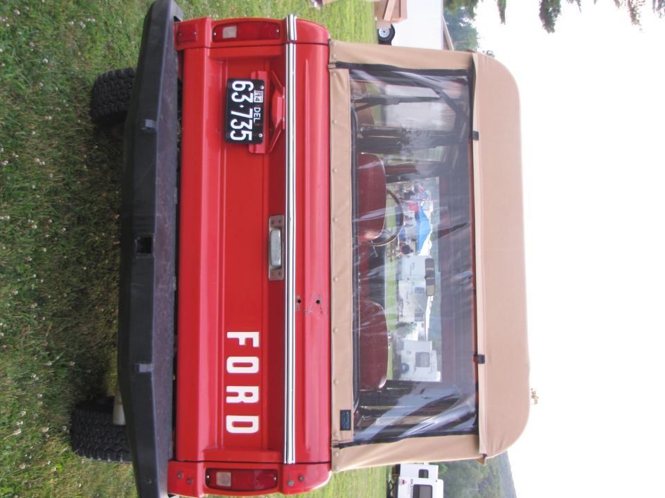 Rear view of a red Ford Bronco with a tan soft top and a Delaware license plate reading 63-735