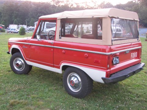 1979 Ford Bronco - This 1979 Ford Bronco is red with a white lower body and a tan soft top, parked outdoors.