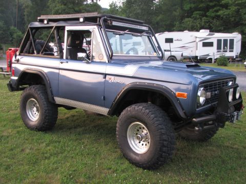 1979 Ford Bronco - A modified 1978 Ford Bronco is shown with a roll cage and off-road tires, parked on a grassy area.