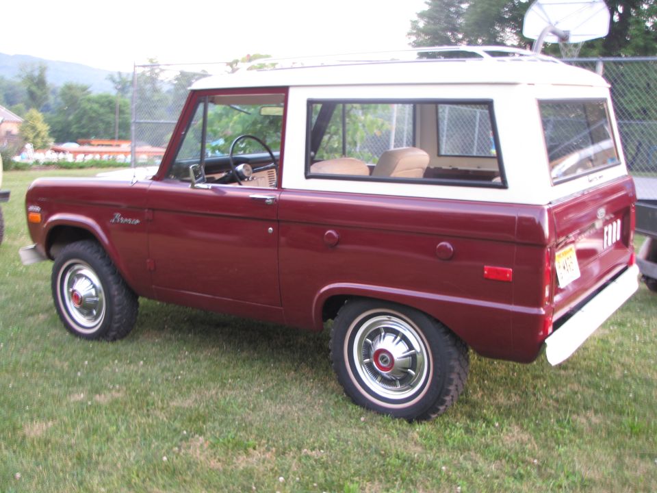 Maroon and white Ford Bronco parked on grass. "Bronco" script on fender