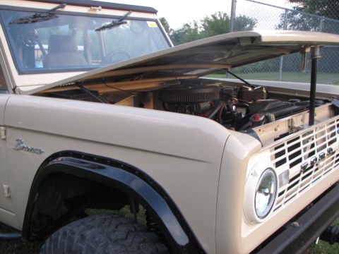 1979 Ford Bronco - The engine bay of a tan Ford Bronco is visible with the hood propped open.
