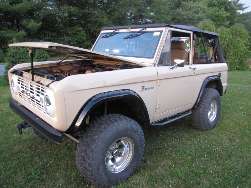 Tan Ford Bronco with hood open, showing engine. Off-road tires and black fender flares