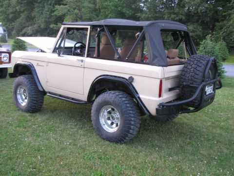 1979 Ford Bronco - This tan 1979 Ford Bronco features a black soft top and a rear-mounted spare tire, parked on a grassy lawn.