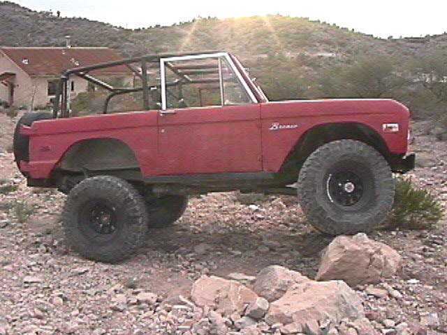 Red topless early Ford Bronco with roll cage on rocky desert terrain