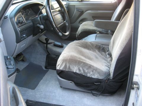 1994 Ford Bronco - The interior of a truck shows the driver's side dashboard, steering wheel, and front seats with covers.
