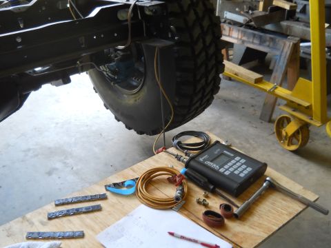 1992 Ford Bronco - Diagnostic equipment and wheel weights are laid out on a workbench next to a vehicle's frame and tire.