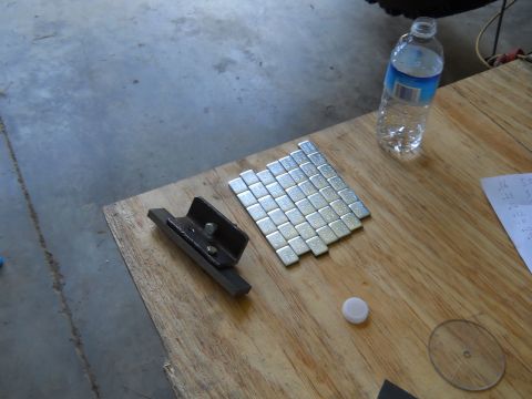 1992 Ford Bronco - A collection of wheel weights and a bracket are laid out on a wooden surface next to a bottle of water.