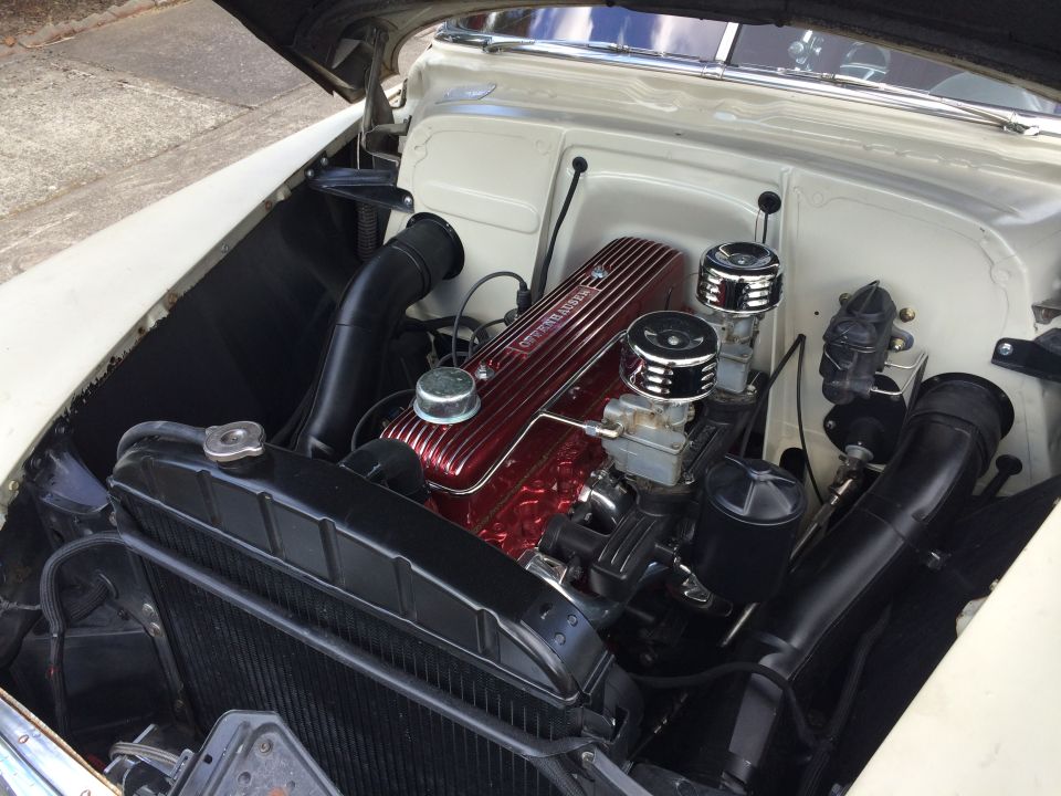 Close-up of a car engine with a red valve cover and dual carburetors