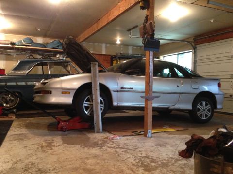 1990 Geo Storm GSi - A silver coupe is being worked on in a garage, with another classic car parked behind it.