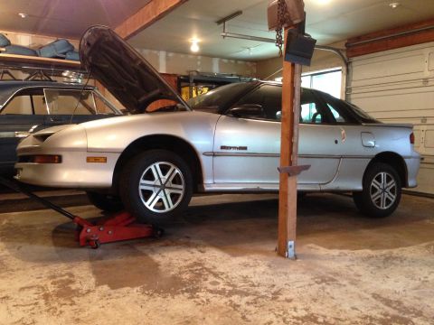 1990 Geo Storm GSi - A silver coupe is being worked on in a garage, with its hood raised and supported by a jack.
