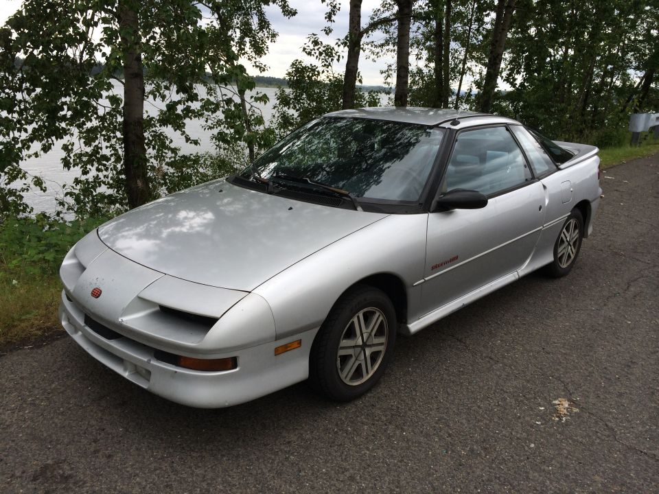 Silver coupe with a black spoiler parked by a lake