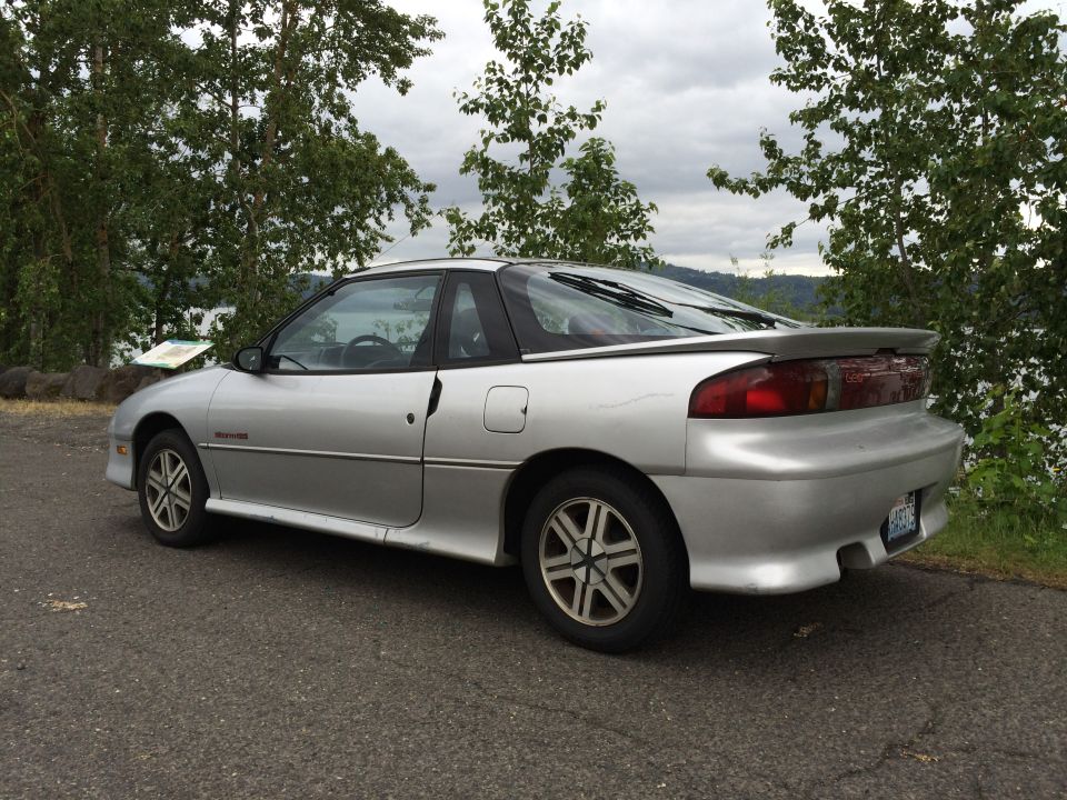 Silver 1990 Geo Storm GSi coupe parked on asphalt with trees and water in background