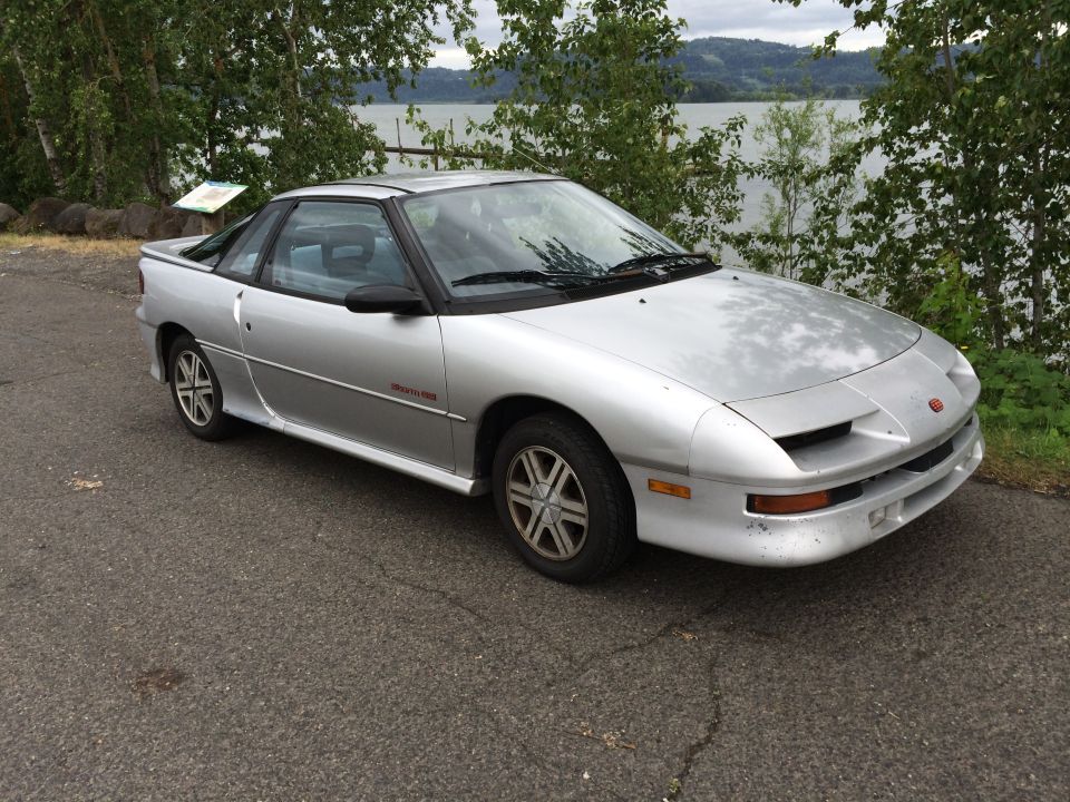 Silver 1990 Geo Storm GSi coupe parked by a lake
