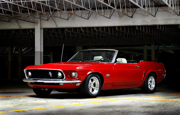 Red convertible Mustang parked inside a garage. It has a black grille and chrome wheels