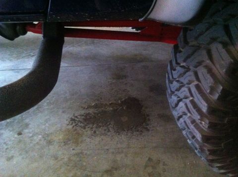 1982 Ford Bronco - A puddle of fluid is visible on the garage floor beneath the vehicle's undercarriage and tire.