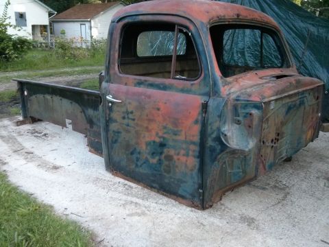 1986 Ford Bronco - This heavily rusted pickup truck cab and bed is missing its grille and windshield.