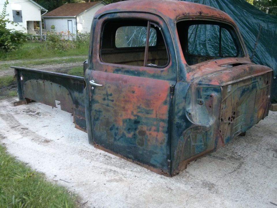 Rusted pickup truck cab and bed, weathered blue and orange paint, missing grille and windshield