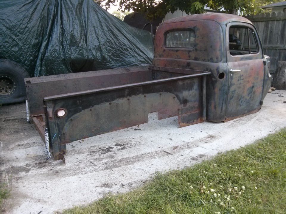 Rusty pickup truck cab and bed sitting on concrete, partially covered by a tarp