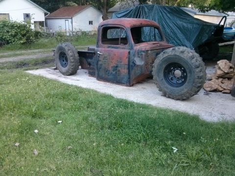 1986 Ford Bronco - A rusty pickup truck cab sits on oversized tires in a grassy yard.