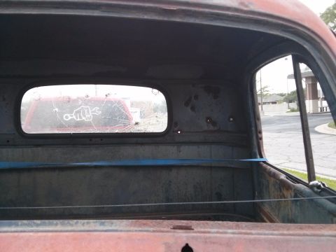 1986 Ford Bronco - View from inside a rusty truck cab, looking through a broken rear window at another vehicle.
