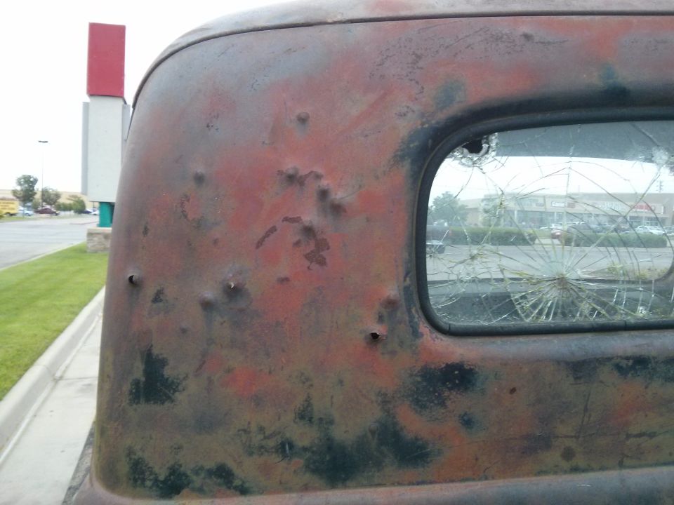 Rusted truck side with bullet holes and shattered rear window