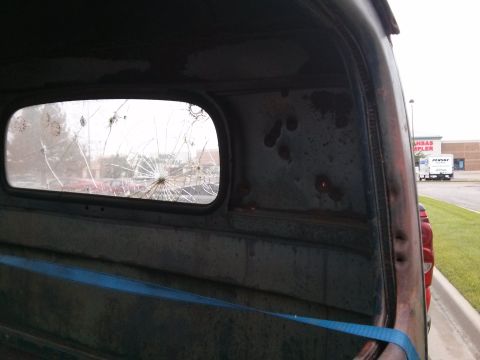 1986 Ford Bronco - The cracked rear window of a truck cab reveals a glimpse of the exterior and a distant building.