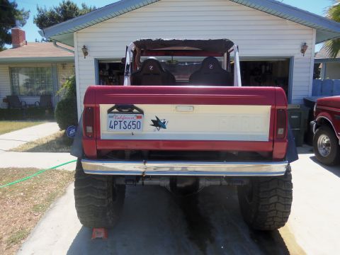 1968 Ford Bronco - Rear view of a red and white Ford Bronco with a California license plate, parked in front of a garage.