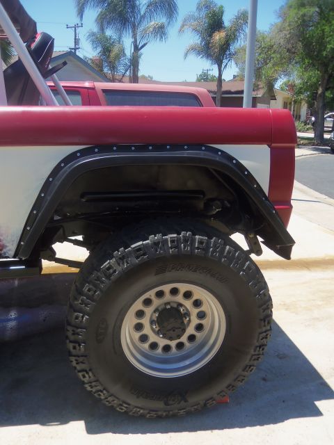 1968 Ford Bronco - A red and white SUV's rear fender and tire are visible, with another vehicle behind it.