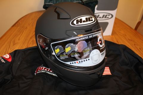 2003 Ford Crown Victoria - matte black HJC full-face helmet with its visor still bearing the spec sticker, placed on a black racing jacket.