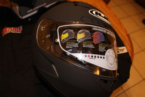 2003 Ford Crown Victoria - matte black HJC helmet sits on a wooden table, its visor bearing a detailed sticker describing pinlock and ventilation features.