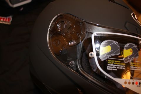 2003 Ford Crown Victoria - Close-up of the interior visor pivot mechanism and mounting hardware of a matte black helmet, with the spec sticker visible.