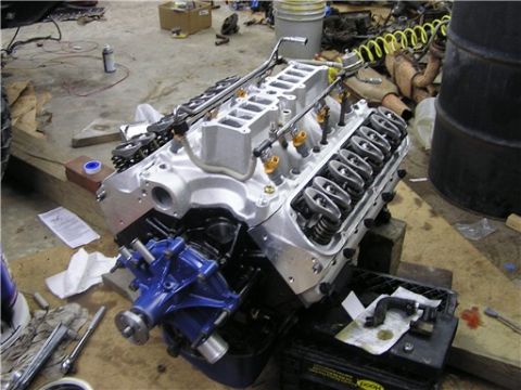 1993 Ford Bronco - A rebuilt engine sits on a stand in a garage, surrounded by tools and parts.