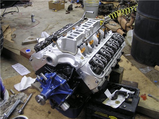 Silver V8 engine on a stand with blue timing cover, aluminum lower intake and exposed rockers