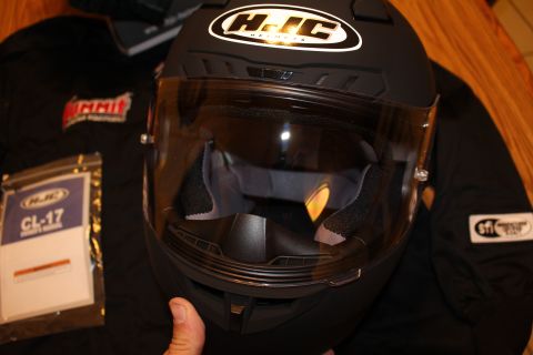 2003 Ford Crown Victoria - Front view of a matte black HJC full-face helmet with the clear shield up, resting on a jacket beside an HJC CL-17 manual.