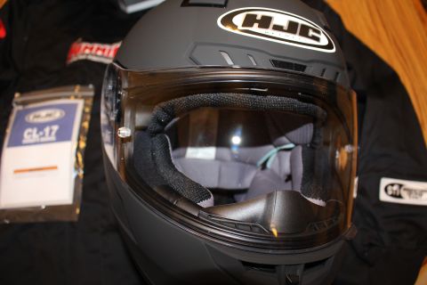 2003 Ford Crown Victoria - matte black HJC full-face motorcycle helmet with clear shield lowered, displayed on a dark jacket.