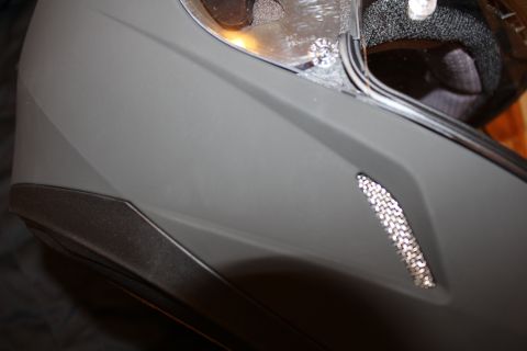 2003 Ford Crown Victoria - Detail of the side and lower chin area of a matte gray full-face helmet showing a mesh-covered intake vent.