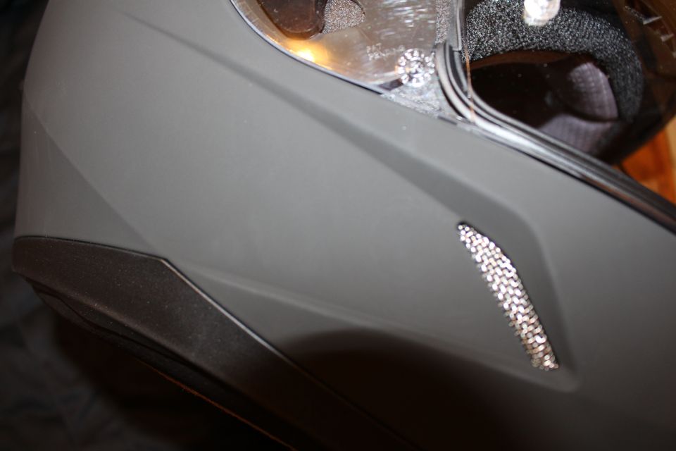 Close-up of a matte gray helmet side vent and lower edge with mesh insert