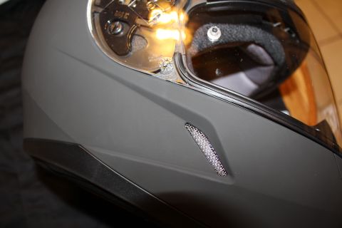 2003 Ford Crown Victoria - Detail of a matte gray full-face helmet showing the shield pivot, lower edge trim and a mesh side vent.