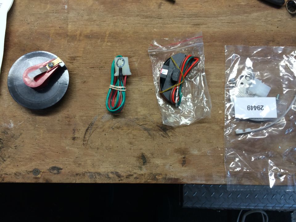 Distributor rotor, wiring harness, and ignition module parts laid out on a wooden workbench