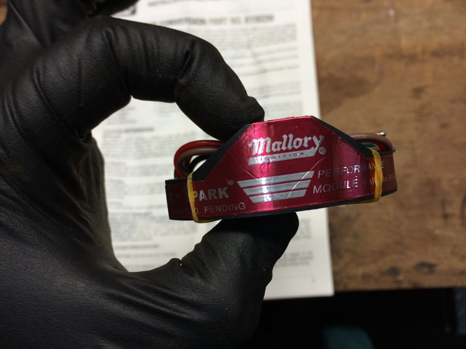 Mallory Ignition performance module held by a gloved hand, with installation instructions in the background