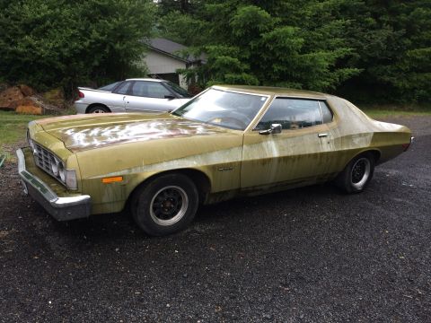 1973 Ford Torino - A faded green 1973 Ford Torino sits parked next to another vehicle in a driveway.