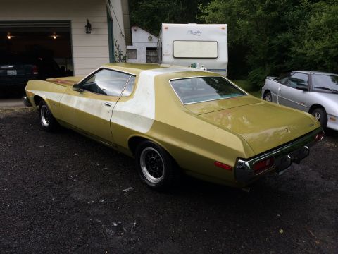1973 Ford Torino - A gold 1973 Ford Torino with a white stripe is parked in a driveway next to a silver sports car and a trailer.