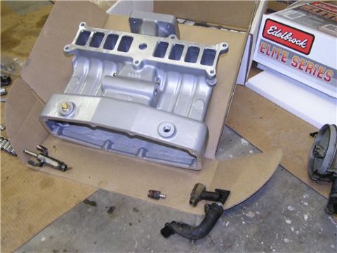 1993 Ford Bronco - Engine intake manifold and associated parts laid out on cardboard, with an Edelbrock box in the background.