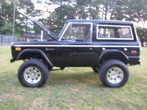 1979 Ford Bronco - This black Ford Bronco is shown from the side with its hood up, revealing a lifted suspension and custom wheels.