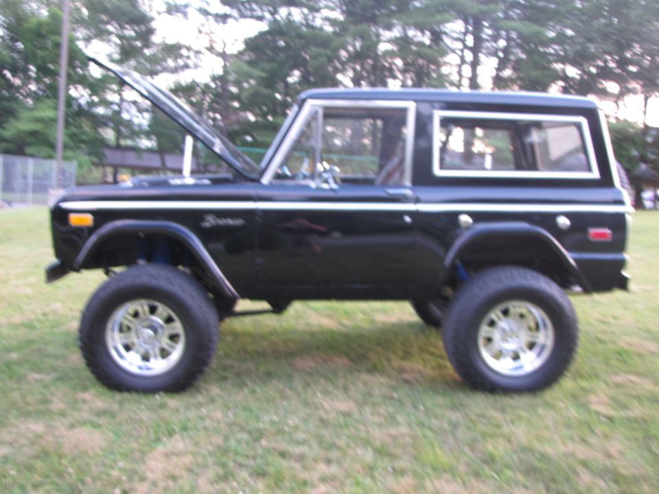 Black Ford Bronco with hood open, lifted suspension, and aftermarket wheels parked on grass