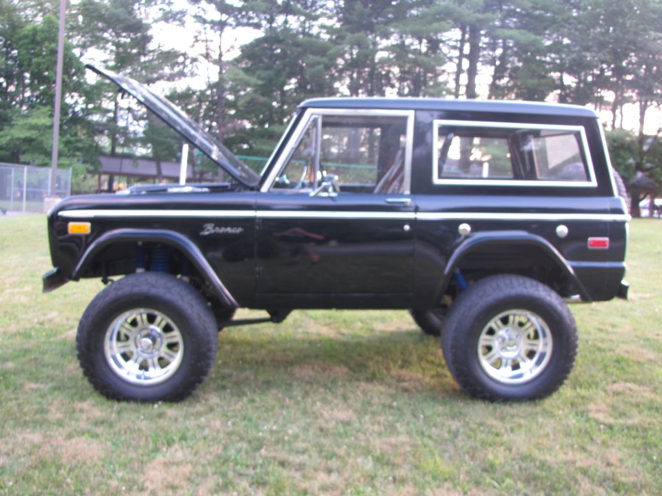 Black 1978 Ford Bronco with hood open, lifted suspension, and chrome wheels parked on grass