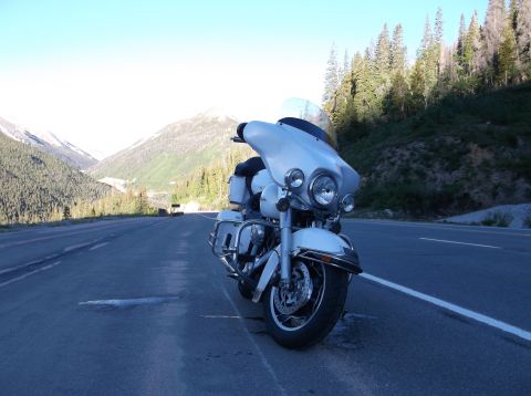 2009 Kenworth T800 - A white motorcycle is parked on the shoulder of a scenic mountain road with pine trees and mountains in the background.