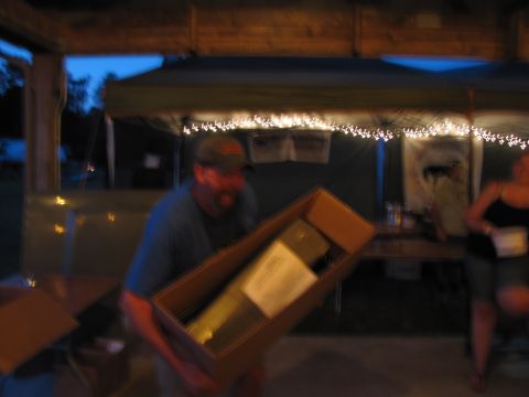 1979 Ford Bronco - A man carries a box containing a long item at an outdoor gathering with string lights overhead.